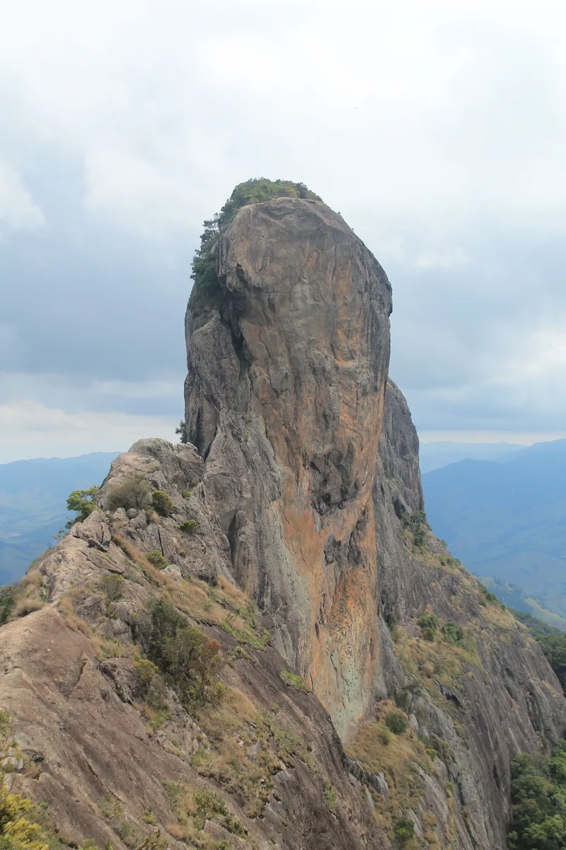 The rock monolith of Pedra do Baú rising above a ridge, with the Mantiqueira mountains and clouds behind it.