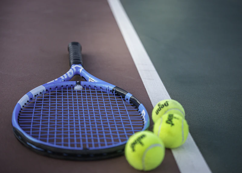 Blue racket and three tennis balls beside the line of a court.